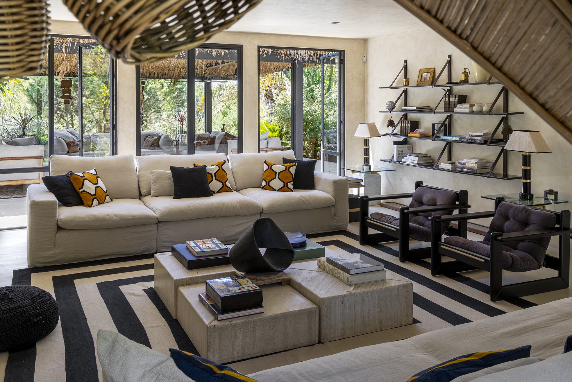 Living room with deep linen sofa, black lounge chairs, iron shelving and open doors to the pergola