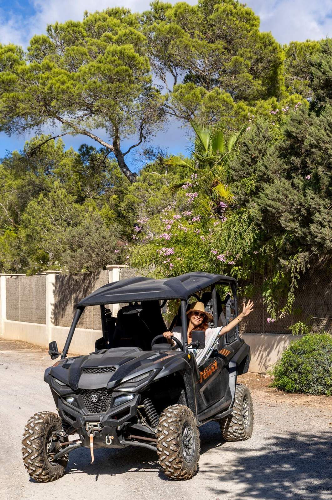Off-road buggy parked on the drive beneath palms and flowering shrubs at the edge of the garden