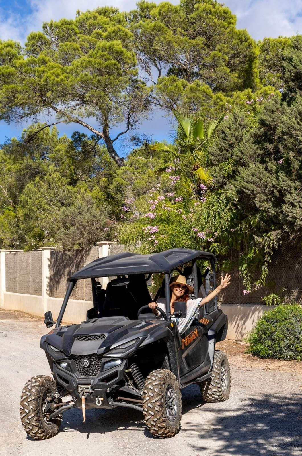 Off-road buggy parked on the drive beneath palms and flowering shrubs at the edge of the garden