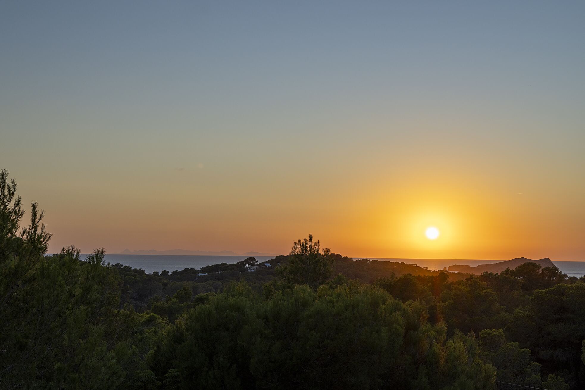 Wide view of the sun setting over the sea with the silhouette of Es Vedrà on the horizon