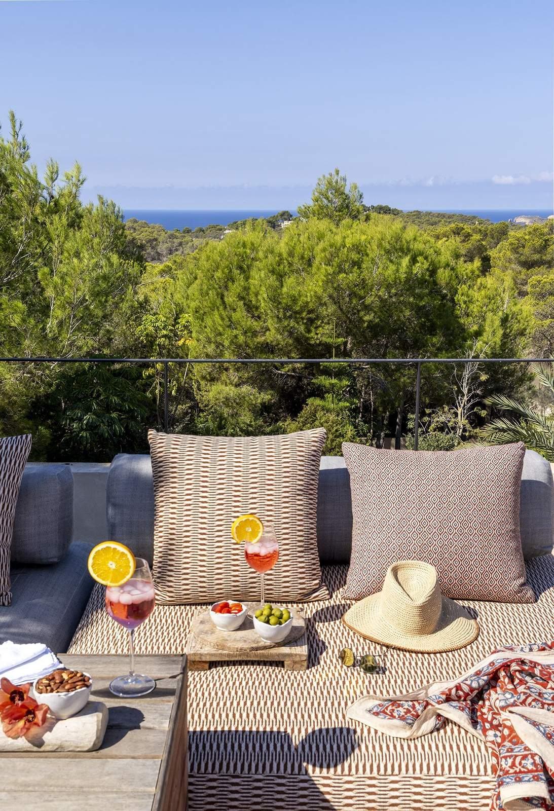 Two spritz cocktails, olives and a straw hat on a terrace daybed with sea view