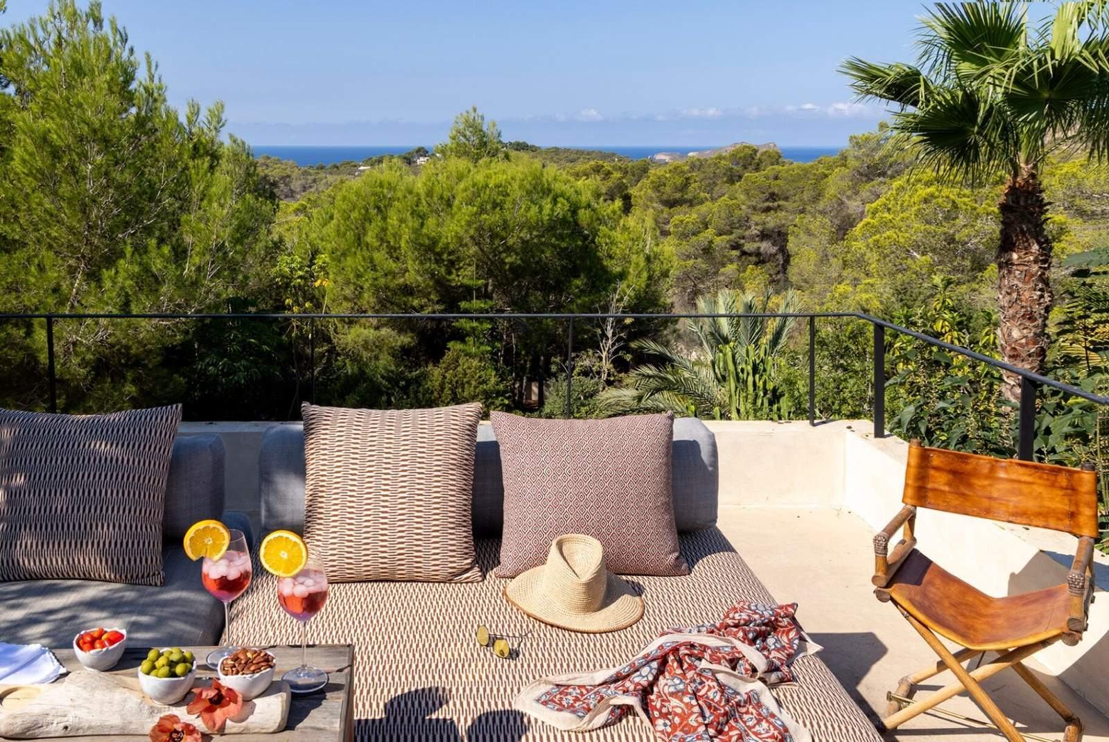 Outdoor sofa with patterned cushions on a terrace overlooking pines, palms and the sea