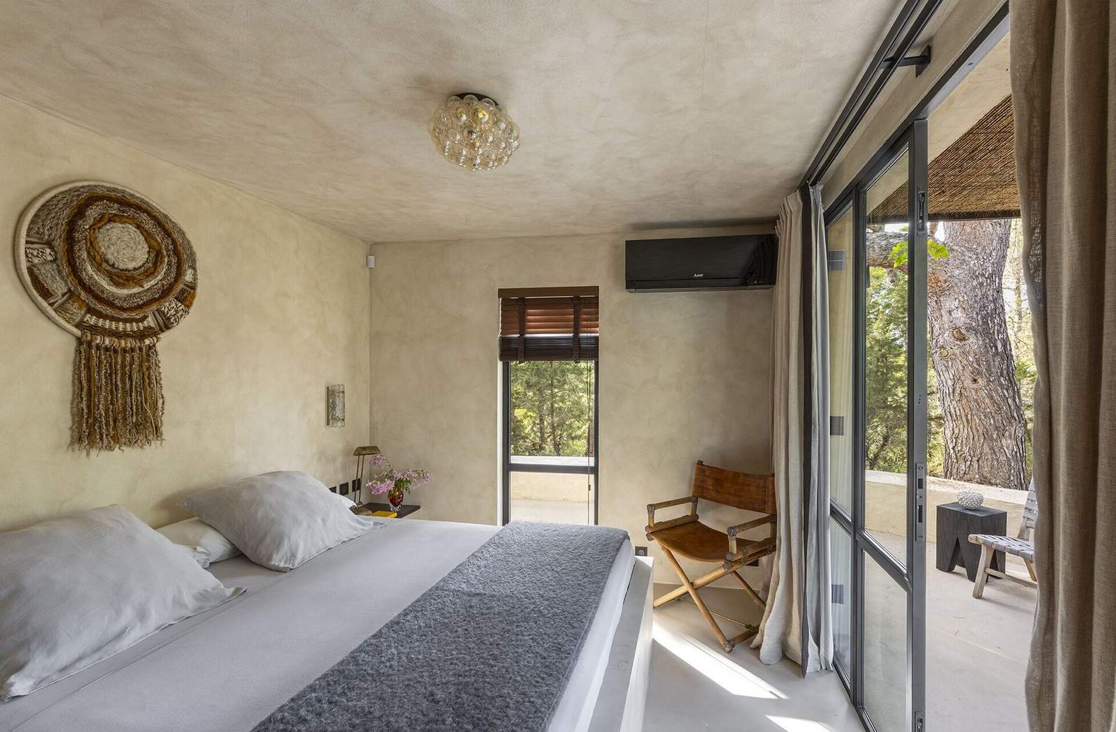 Bedroom interior with circular jute wall hanging and steel doors to terrace