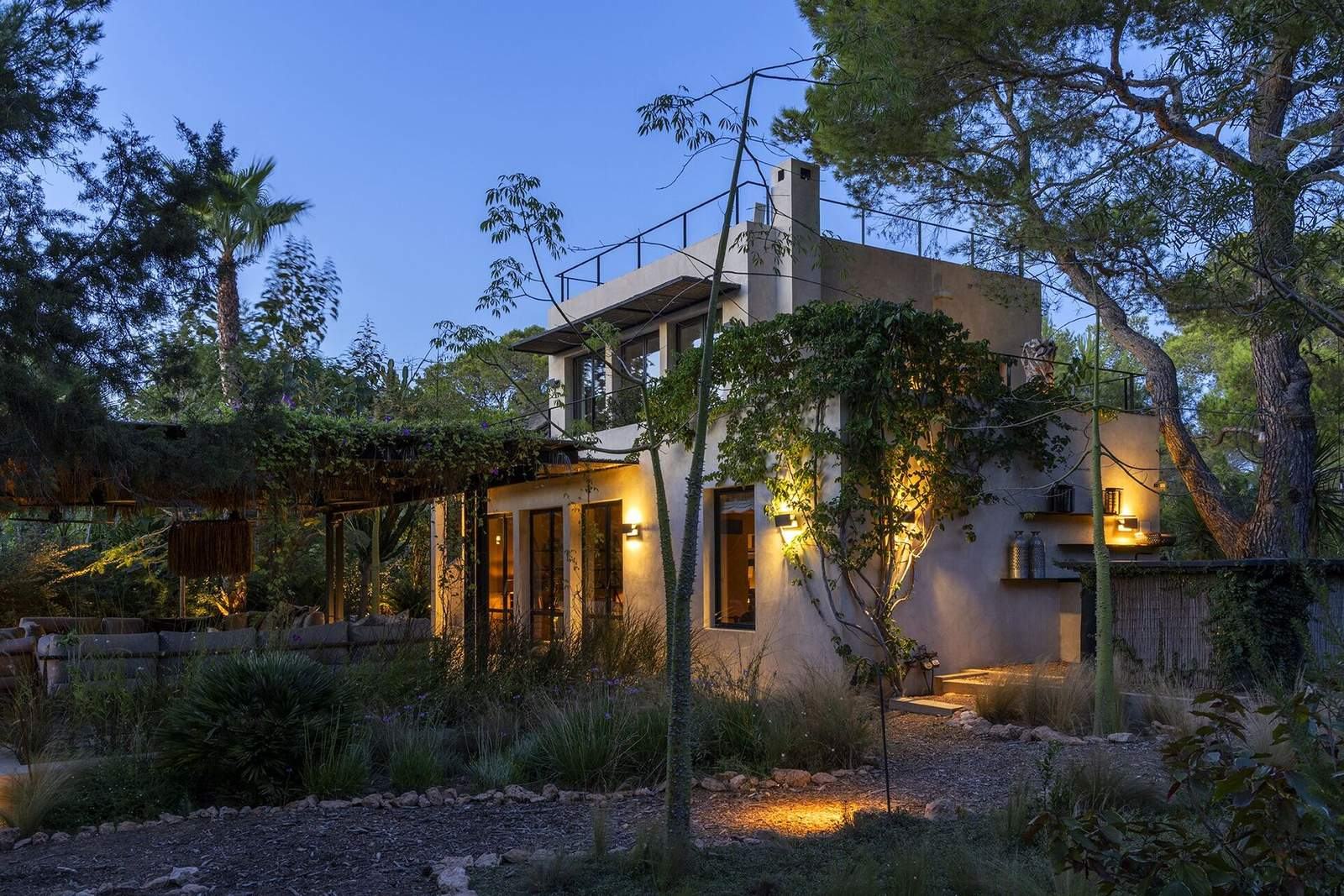 Guest house exterior at dusk glowing among palms and pines