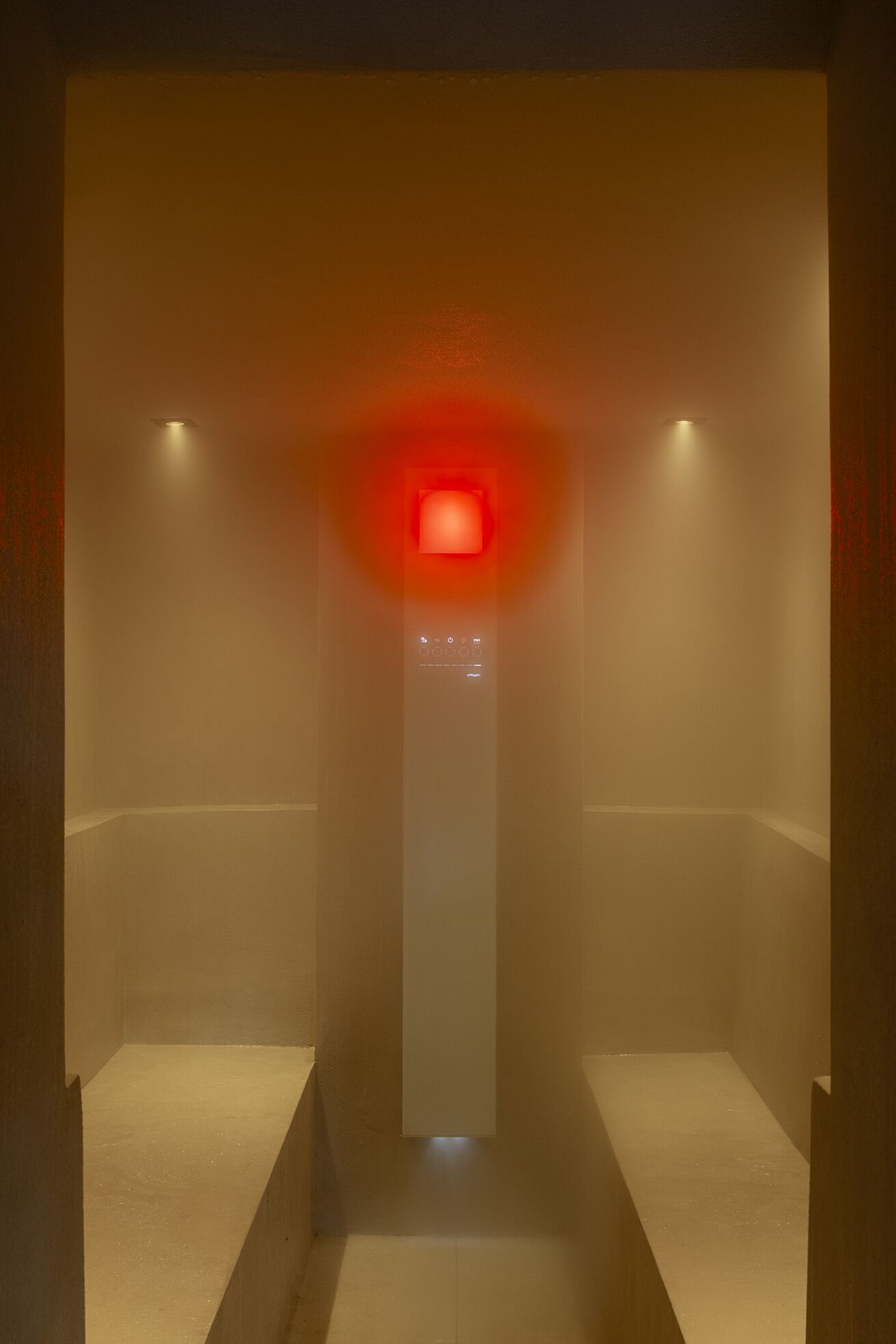 Tadelakt hammam steam room with heated stone benches and a red chromotherapy lamp glowing through the steam