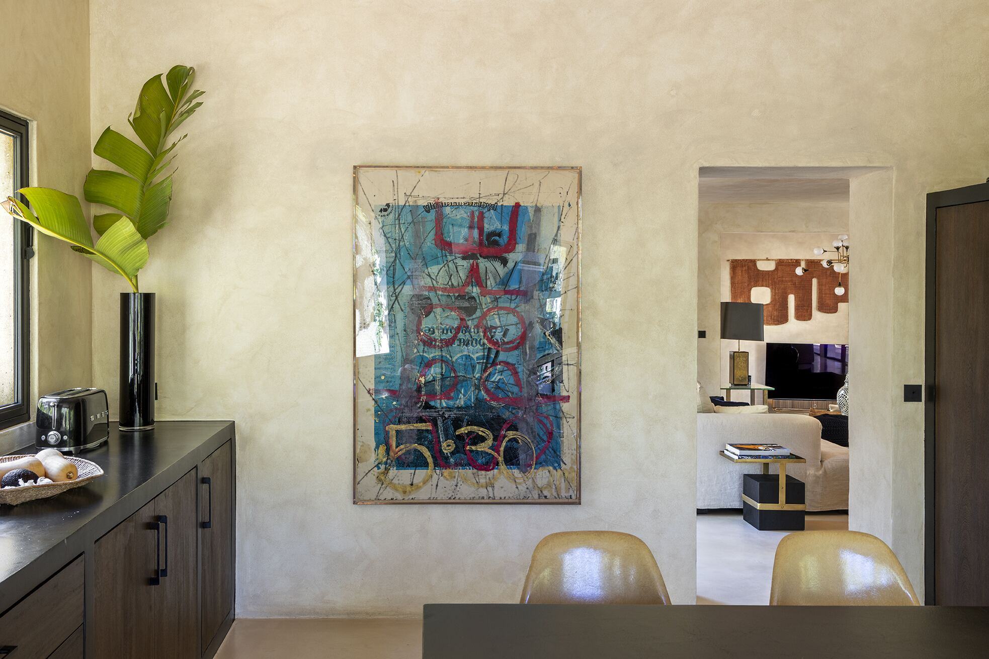 Lime-washed kitchen wall with large abstract artwork and view through to the living room