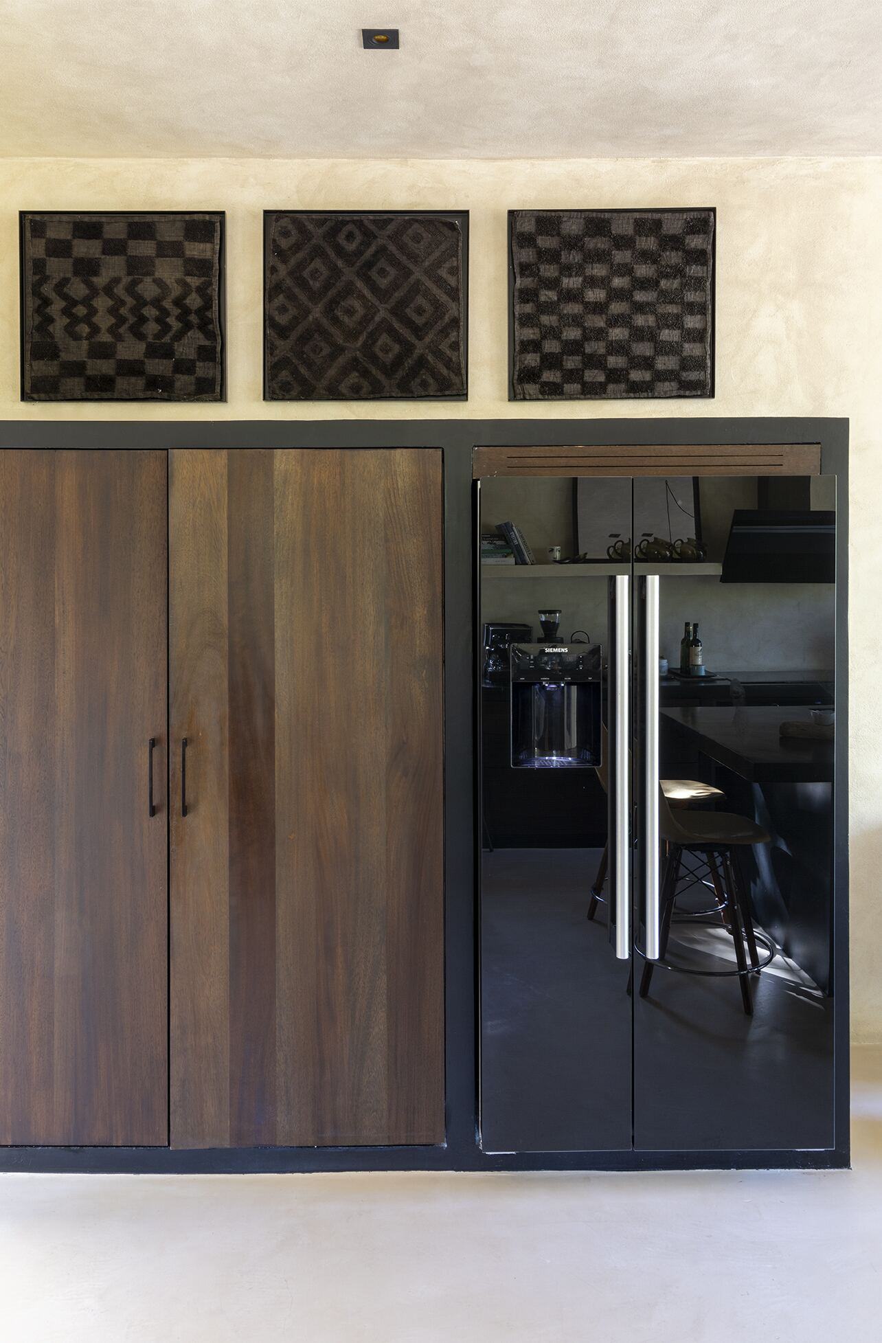Walnut kitchen cabinetry with integrated black fridge and framed textile art above