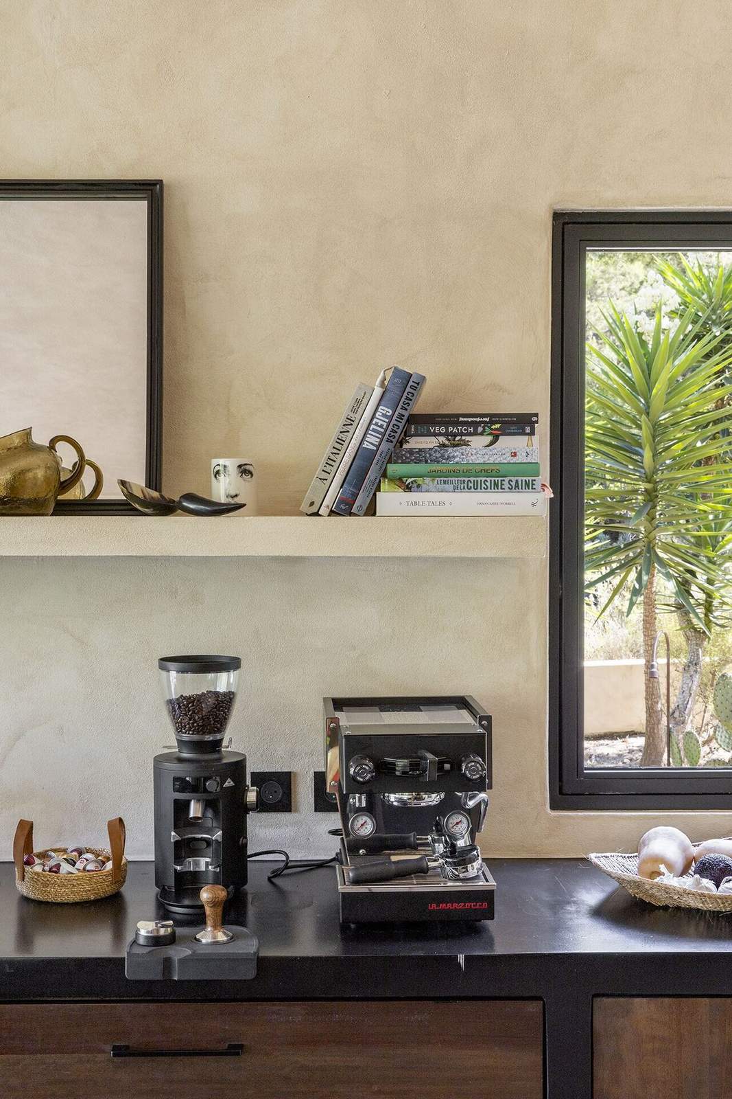 Black countertop with espresso machine, grinder and a shelf of cookbooks
