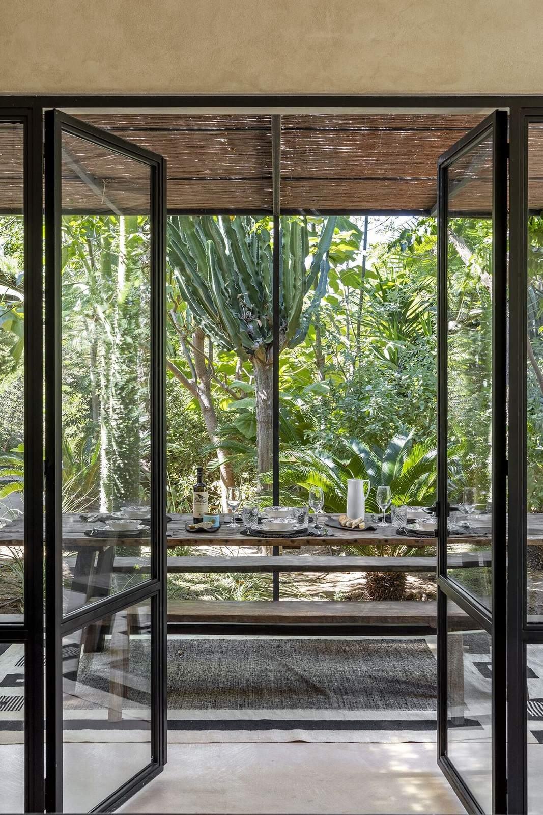 View through open steel-framed doors to the outdoor dining table and a tall cactus