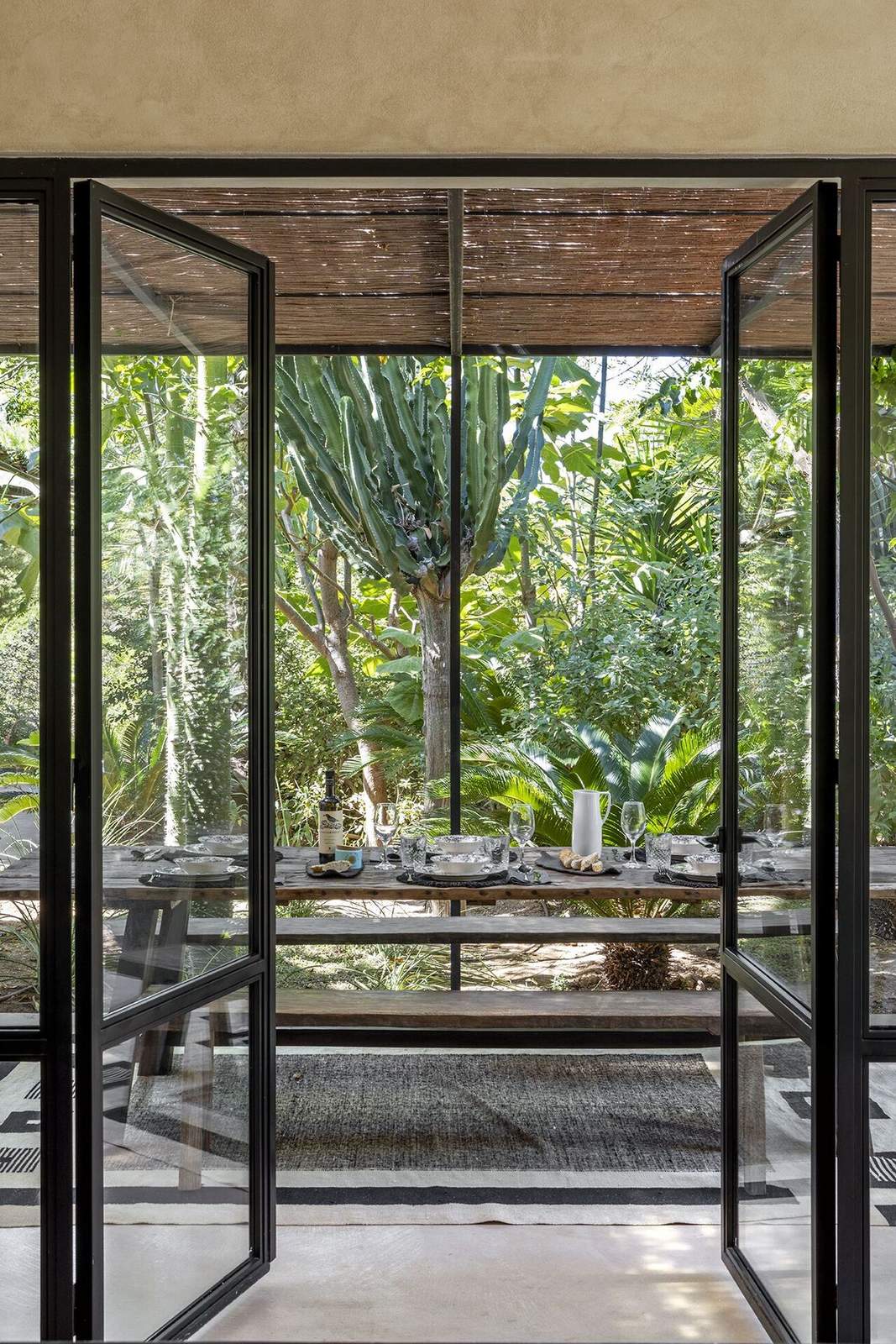 View through open steel-framed doors to the outdoor dining table and a tall cactus