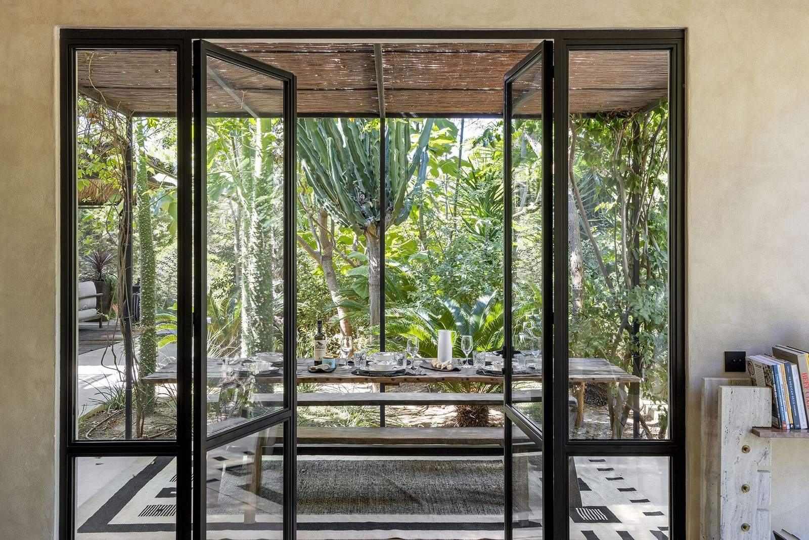 Steel-framed glass doors opening onto the rustic outdoor dining table in the garden
