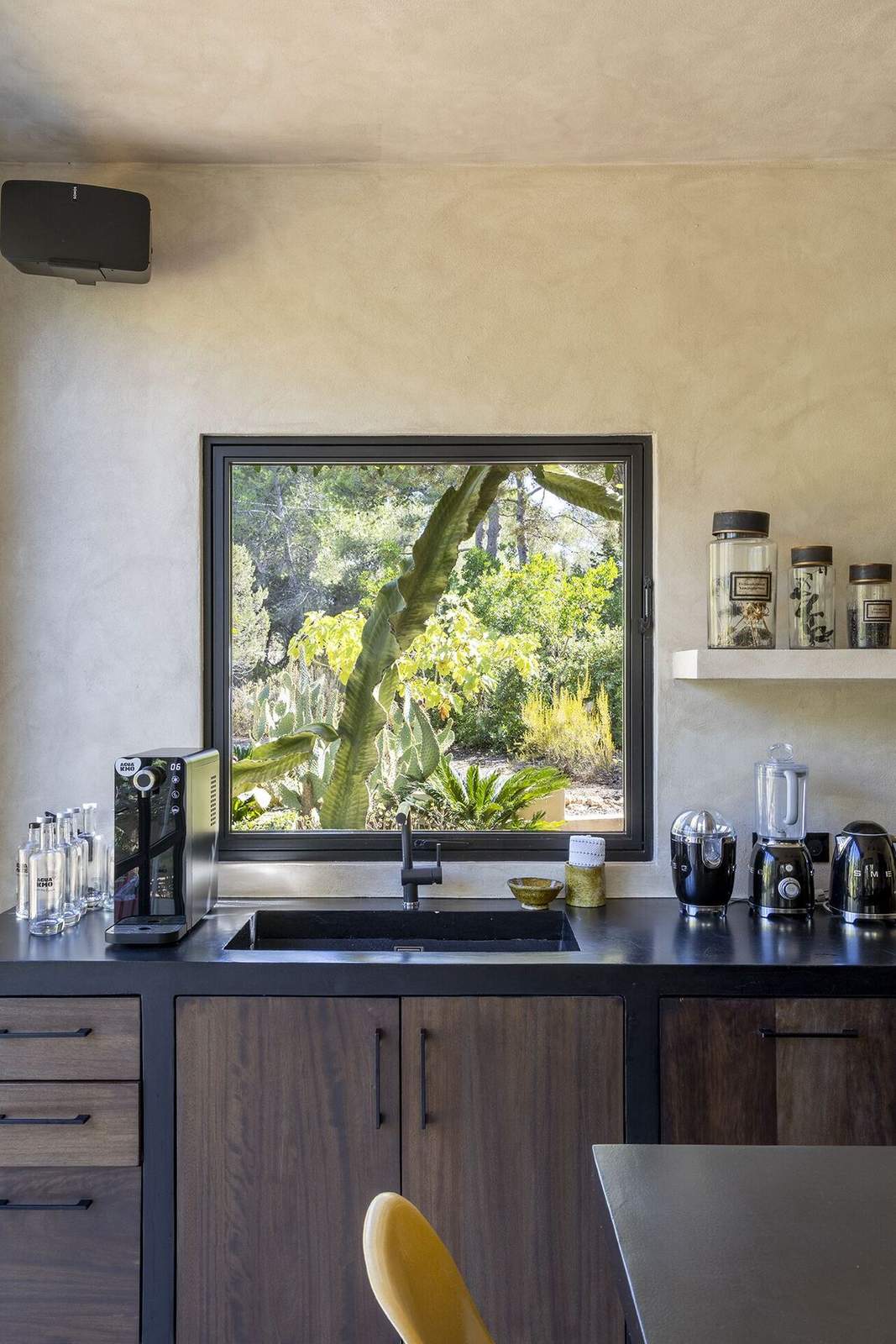 Kitchen sink and black counter set below a large window looking onto the garden