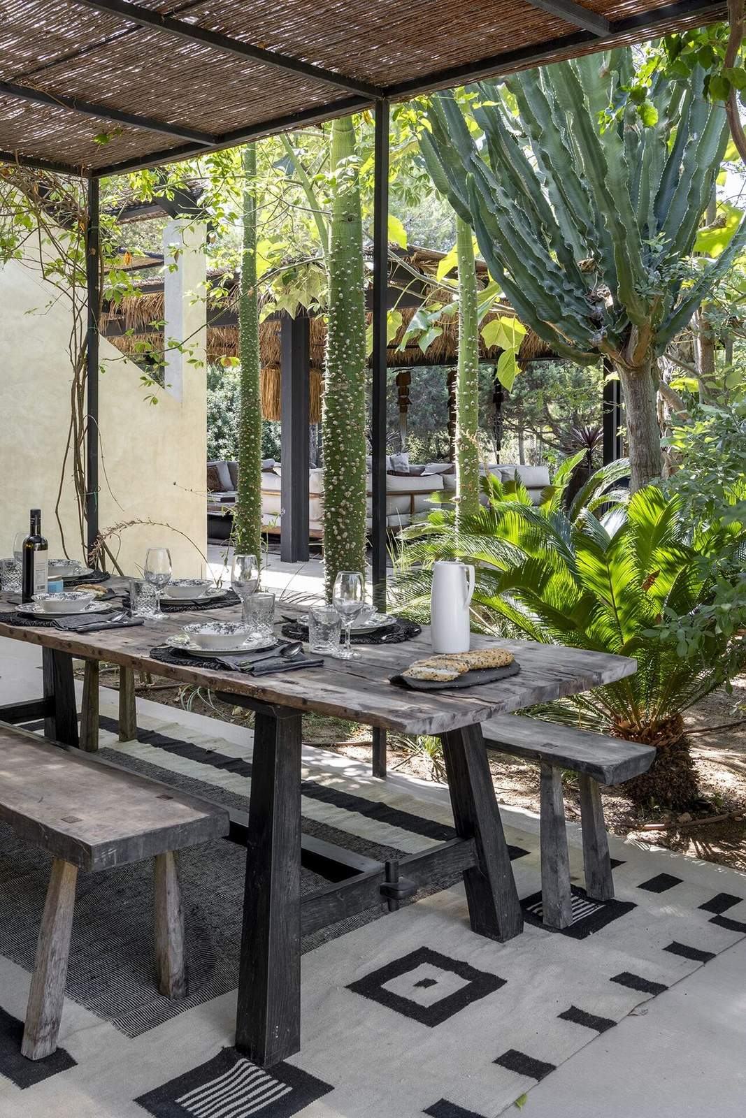 Outdoor dining table set for lunch under a reed pergola surrounded by tall cactus