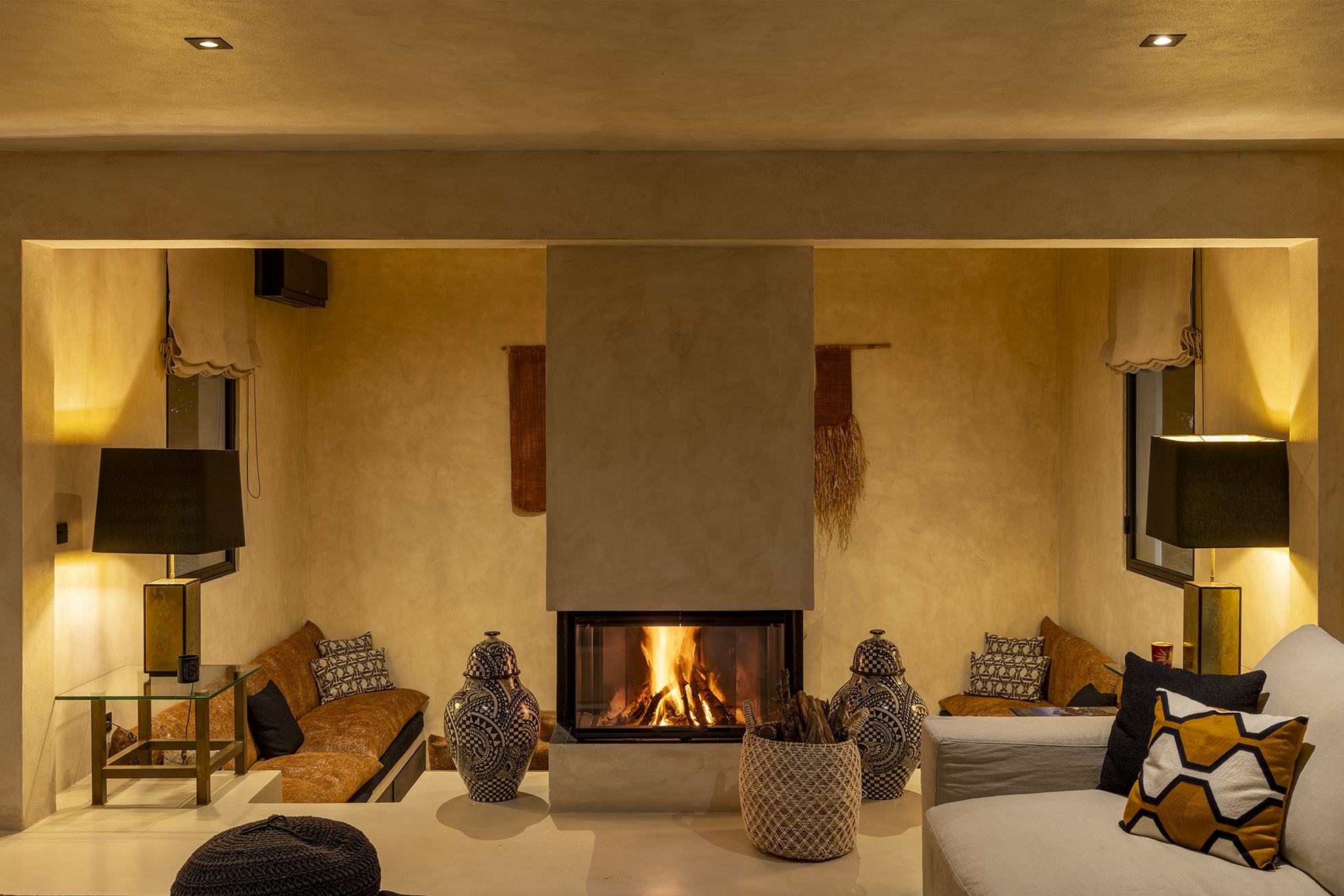 The stone fireplace in the Can Serenico living room lit on a winter evening, the fire glowing against the dark pines of Ibiza