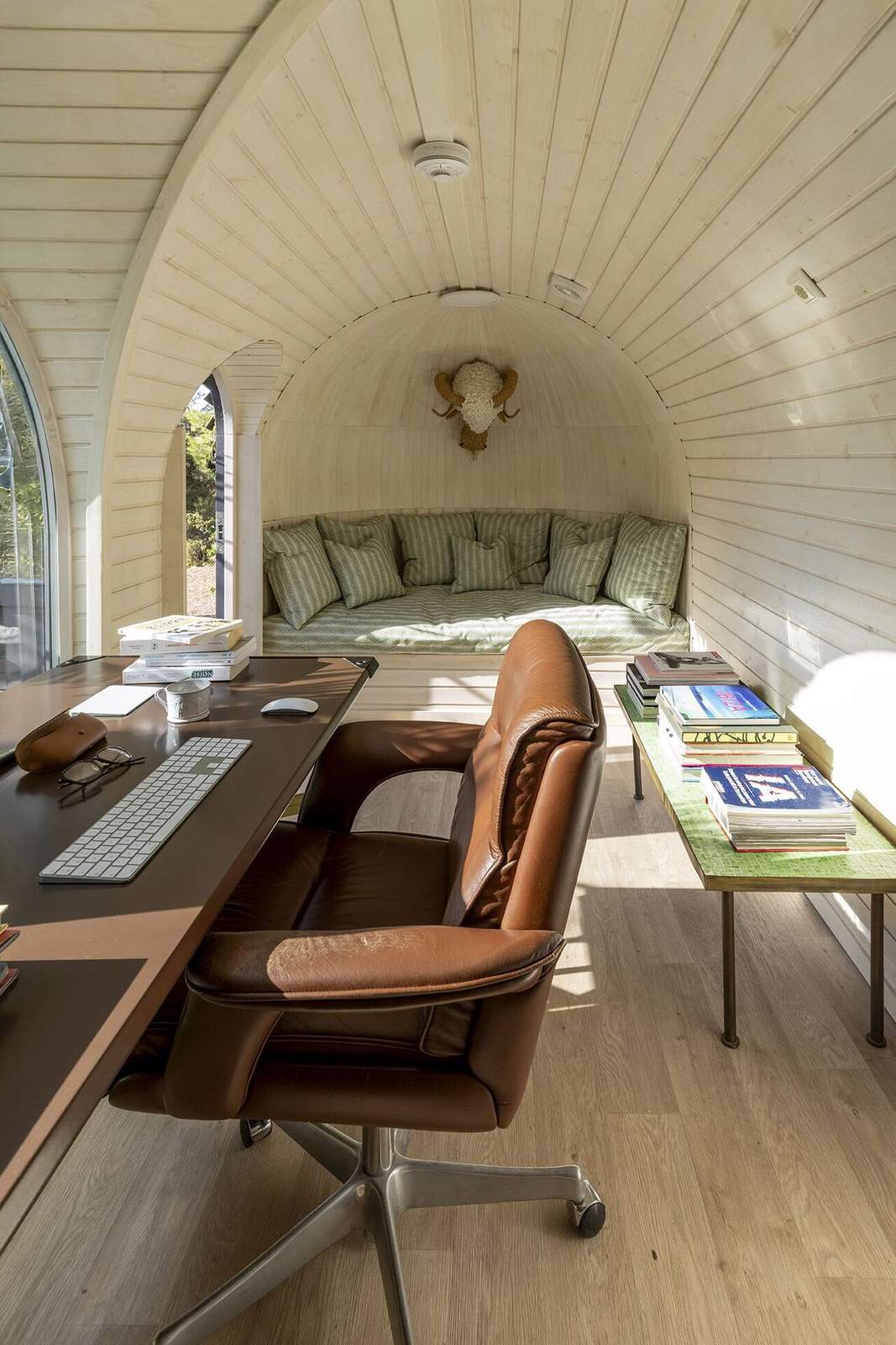 Pale wood interior of the igloo office with desk, brown leather chair and herringbone-cushioned daybed