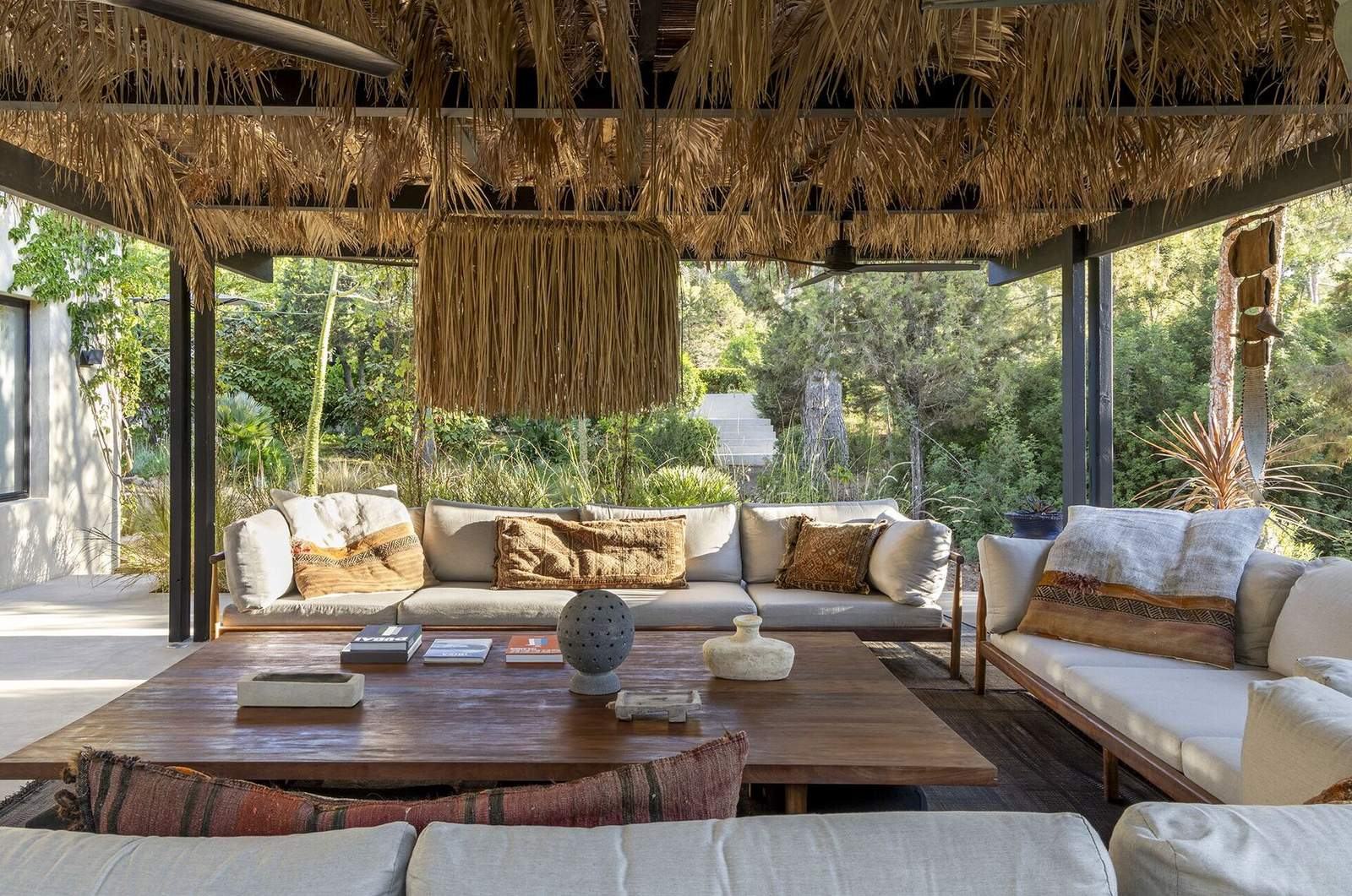 Outdoor pergola lounge with raffia chandelier, linen sofas and view onto wild Mediterranean garden