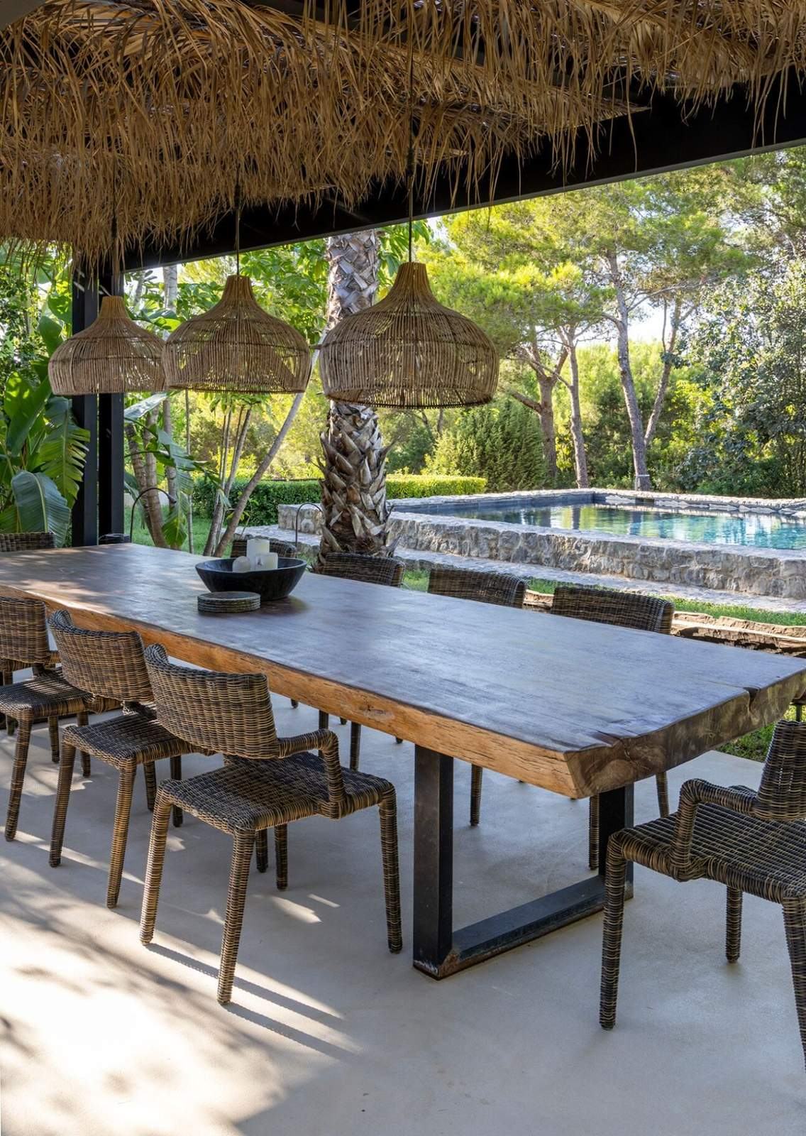 Live-edge dining table under woven lanterns with the stone-edged pool beyond