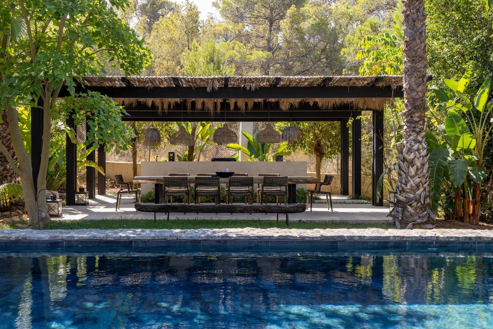 Thatched pergola with long dining table reflected in the turquoise pool