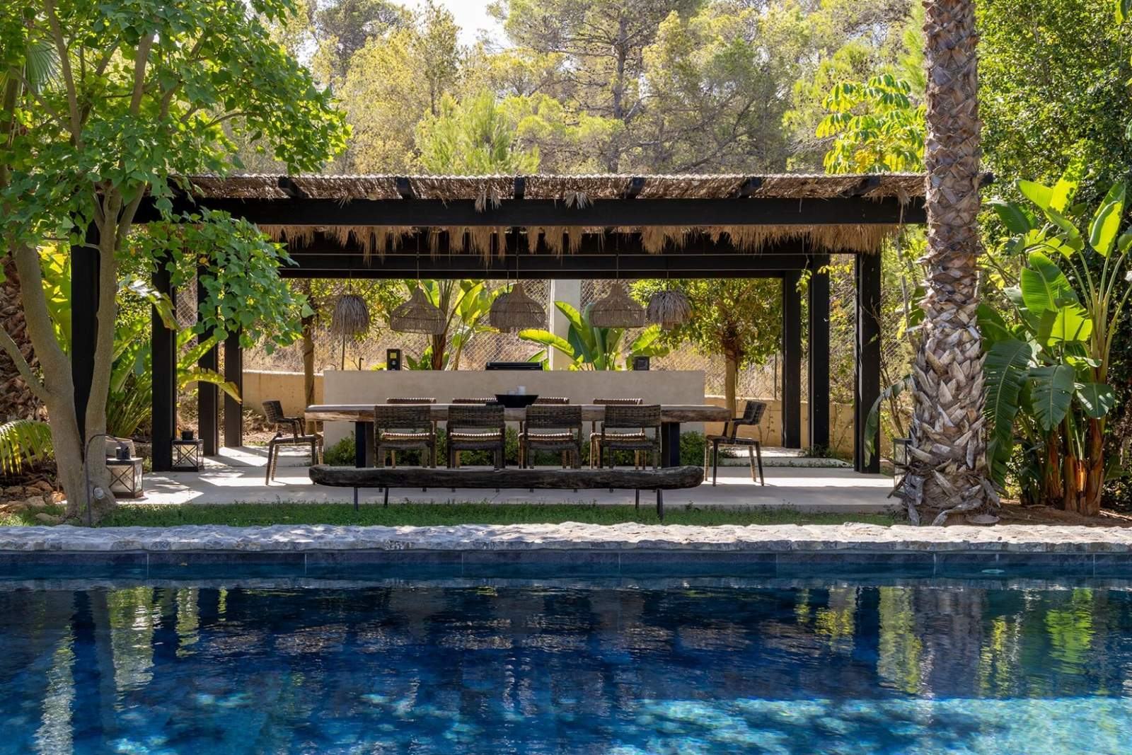 Thatched pergola with long dining table reflected in the turquoise pool