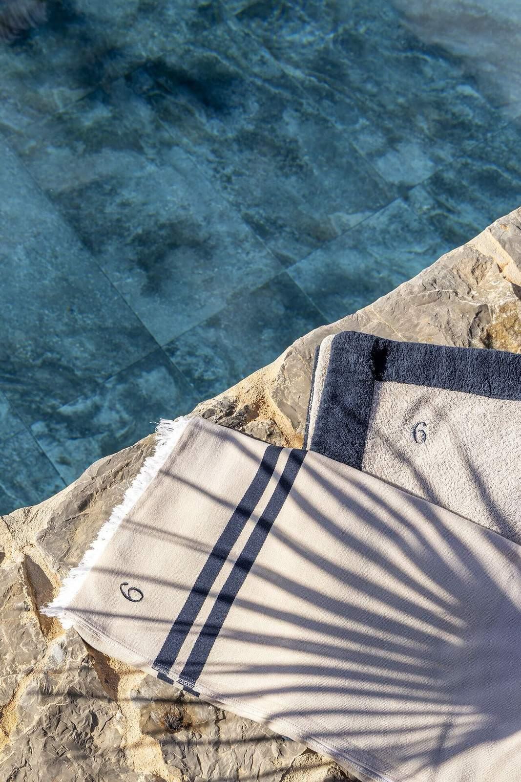 Folded pool towels resting on the stone edge above clear blue water