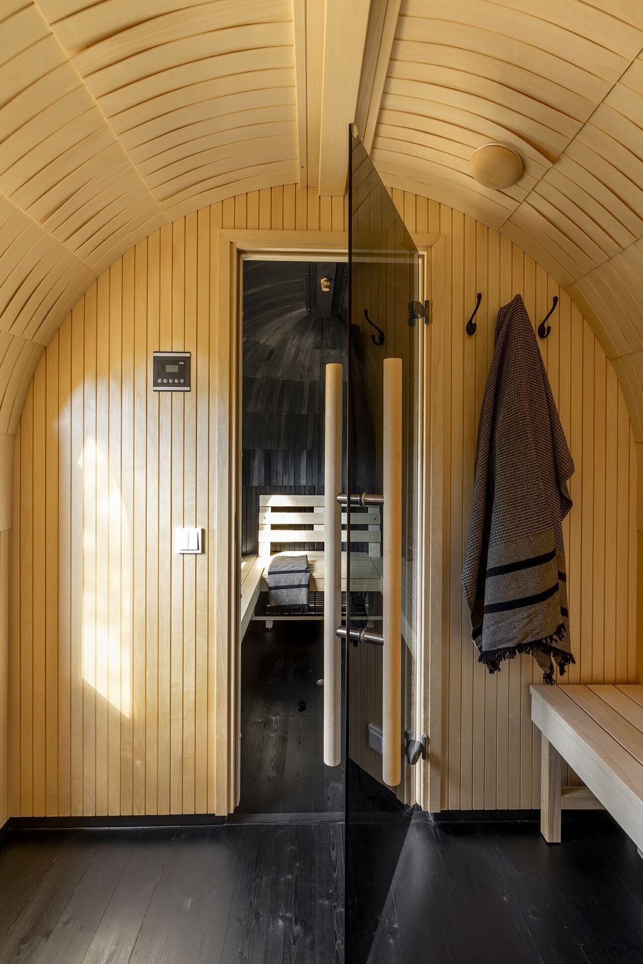 Pale cedar-clad antechamber of the sauna with hooks, towels and glass door