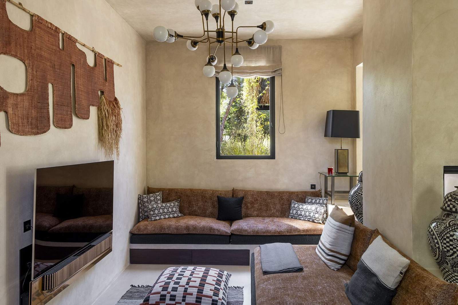 TV room with low rust-toned daybeds, woven wall hanging and brass globe chandelier